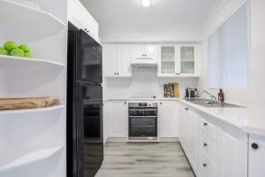 a kitchen with white cabinets and a black refrigerator at Aquamarine - modern & bright Huskisson townhouse in Huskisson