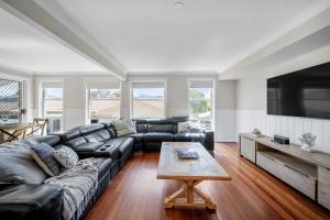 a living room with a black leather couch and a table at Karinya Jervis Bay - 4BR home & optional studio in Vincentia