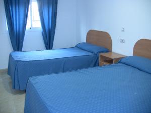 two beds in a hotel room with blue curtains at Apartahotel Los Hermanos in Ocaña