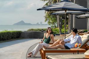 a man and woman sitting on benches under an umbrella at Hua Hin Marriott Resort and Spa in Hua Hin