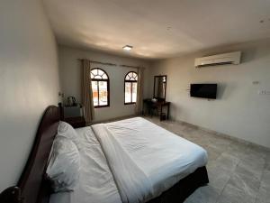 a bedroom with a bed and a tv and two windows at Alreef Hotel Suits in Muscat