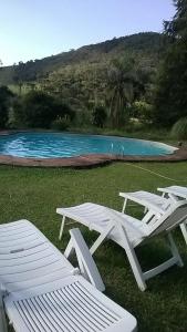 two white chairs and a table next to a swimming pool at Pousada Casa Da Fazenda in Paraisópolis