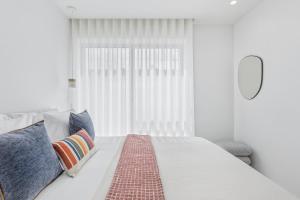 a white bedroom with a bed with pillows and a window at Sal D’Ouro Skyline & Sea Views in Canidelo