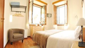 a bedroom with a bed and a chair and two windows at Hospedaria Pielas in Sintra