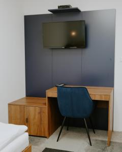 a desk with a blue chair and a television on a wall at ŠD Jedlíkova 9 in Košice