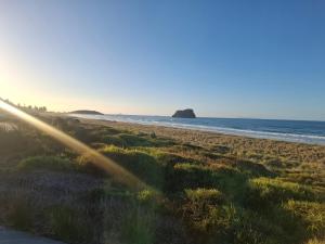 a beach with the sun shining on the sand and the ocean at TuiHideaway cozy studio sleepout in Mount Maunganui