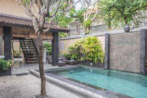 a swimming pool in front of a building with a tree at Villa Karma Legian in Legian +9 photos