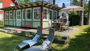a green and white cabin with chairs and an umbrella at Ferienhaus Kienhus in Graal-Müritz +20 photos