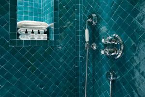 La salle de bains est pourvue d'une douche carrelée de bleu avec un pommeau de douche. dans l'établissement Le Roch Hotel & Spa, à Paris