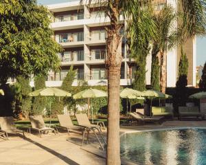 a hotel with chairs and umbrellas next to a swimming pool at Topazio Vibe Beach Hotel & Apartments - Adults Friendly in Albufeira