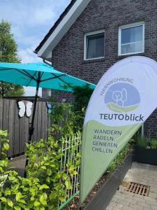 a sign in front of a house with an umbrella at Ferienwohnung Teutoblick Leeden in Tecklenburg