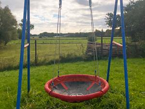 a red swing in the middle of a field at Landhaus Kreitlow in Ribnitz-Damgarten