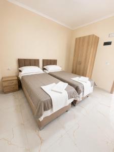 two beds in a bedroom with white walls and marble floors at R&A Apartments in Berat