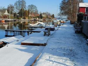 a snow covered path next to a river with boats at Ferienhaus Hieve in Marienwehr