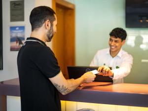 a man standing at a counter holding a remote control at Mercure Florianópolis in Florianópolis