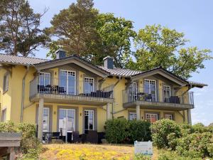 a yellow house with balconies and trees at Haus Strandkiefer in Baabe