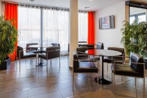 a waiting room with tables and chairs and windows at Hotel H2 Avila in Ávila