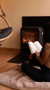 a person reading a book in front of a fireplace at La Cabane du Gardien in Marche-en-Famenne