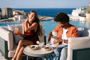 a man and a woman sitting at a table with food at voco Malta by IHG in St. Julianʼs +200 photos