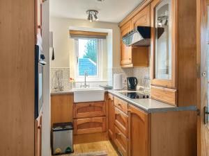 a kitchen with wooden cabinets and a sink and a window at Bothy Cottage - Uk51350 in Peebles