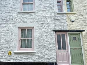 a white building with a pink door and two windows at Gypsett in Polruan