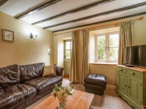 a living room with a leather couch and a tv at Fern Cottage in Bradwell