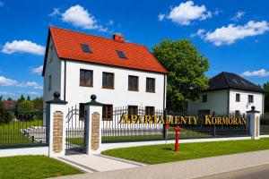 a white house with a red roof behind a fence at Hotel & Restauracja Kormoran in Orzysz