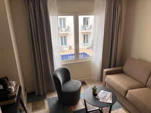 a living room with a couch and a chair and a window at Hôtel Le Yachtman, The Originals Collection in La Rochelle