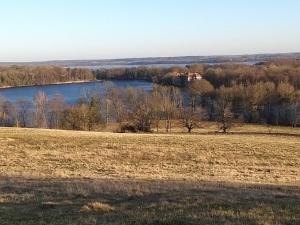 a field with a lake and a house in the distance at Ferienhaus Altes Kabinett in Schorssow