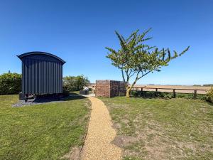a shed in a field with a tree and a fence at Shepherds Hut - Uk49729 in King's Lynn