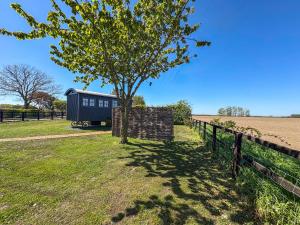 a tree in a field next to a fence at Shepherds Hut - Uk49729 in King's Lynn