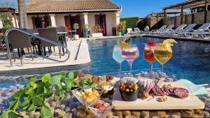 a table with wine glasses and food next to a swimming pool at Hôtel Le Mas Des Amandiers in Graveson