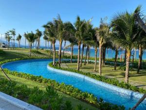 a pool with palm trees and the ocean in the background at Arena jakovi condotel in Cam Lâm