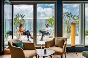 a man and woman sitting in chairs in a room with windows at Hôtel de la Cité in Nantes