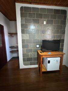 a room with a table with a tv and a brick wall at Pousada famíliar no Centro com café da manhã incluso in São Lourenço