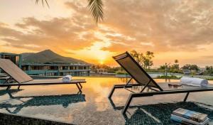 two lounge chairs on a swimming pool at sunset at The Kamala View in Kamala Beach