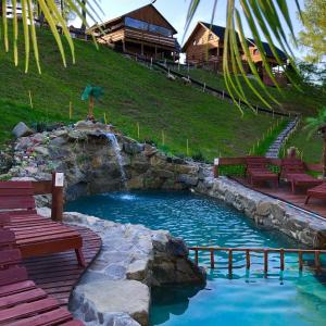a pool with benches and a waterfall in a yard at Agroturystyka Paradiso domki pokoje in Ropa