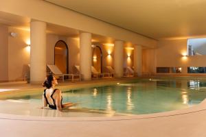 a woman sitting on the edge of a swimming pool at Falésia Hotel - Adults Only in Albufeira