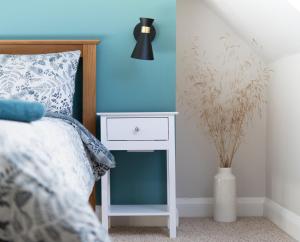 a bed with a white nightstand next to a blue wall at Remore Steading - The Coach House in Ardclach