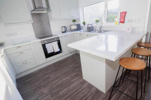 a white kitchen with a counter and stools at Glenroy House Swansea in Swansea +22 photos