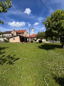 a field of green grass with a building and a tree at GOLD Apartman - Kuća za odmor in Sanski most