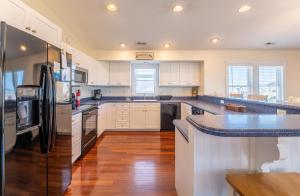 a kitchen with white cabinets and a black refrigerator at Carolina Kai II - Kitty Hawk MP 3, 228 Yards to Beach, Ocean View, Pool, Hot Tub in Kitty Hawk