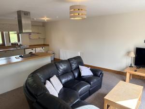 a living room with a leather couch and a kitchen at Abernethys Cottage in Connel