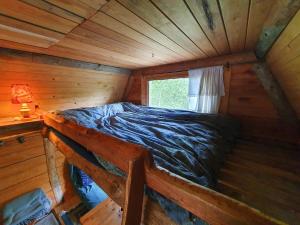 a bed in a wooden cabin with a window at Rustic Cabin on Off-Grid Homestead in Brattfors