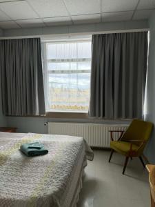 a bedroom with a bed and a chair and a window at Guesthouse Langafit in Laugarbakki