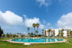 a swimming pool with palm trees and a building at Apto Oasis Playa & Golf Almerimar in Almerimar