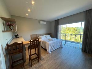 a bedroom with a bed and a desk and a balcony at Suítes Bela Vista in Pomerode