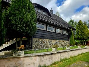 a house with a black roof and a stone wall at Chalupa pod Skleným Vŕškom in Huty