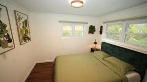 a bedroom with a green bed and two windows at Nemandua Catskills: Hot Tub+Fire Pit+Pool Table+EV in Lanesville