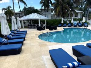 a swimming pool with blue lounge chairs and umbrellas at Beachfront 3Br3Ba Skyyard Ocean Sunset Views, Pool in George Town